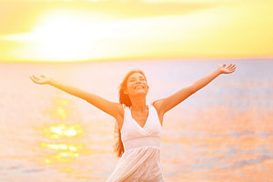 Freedom woman happy and free open arms on beach at sunny sunset. Beautiful joyful elated woman looking up smiling by the ocean during summer holidays vacation. Pretty multiracial Asian Caucasian girl.